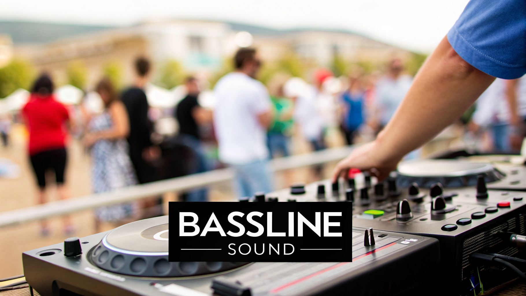 A DJ's hand adjusts controls on a mixing console at an outdoor music event with a blurred crowd.